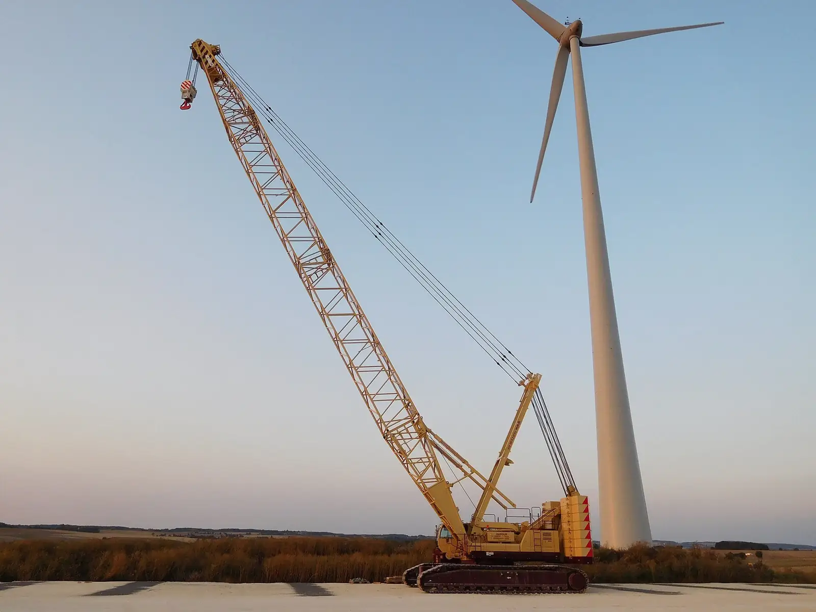 Large crawler crane lifting a wind turbine section against an evening sky
